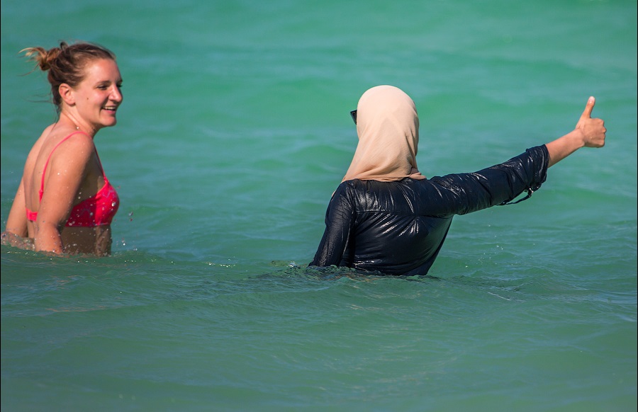 Туристка в бикини и молодая мусульманка в купальнике буркини